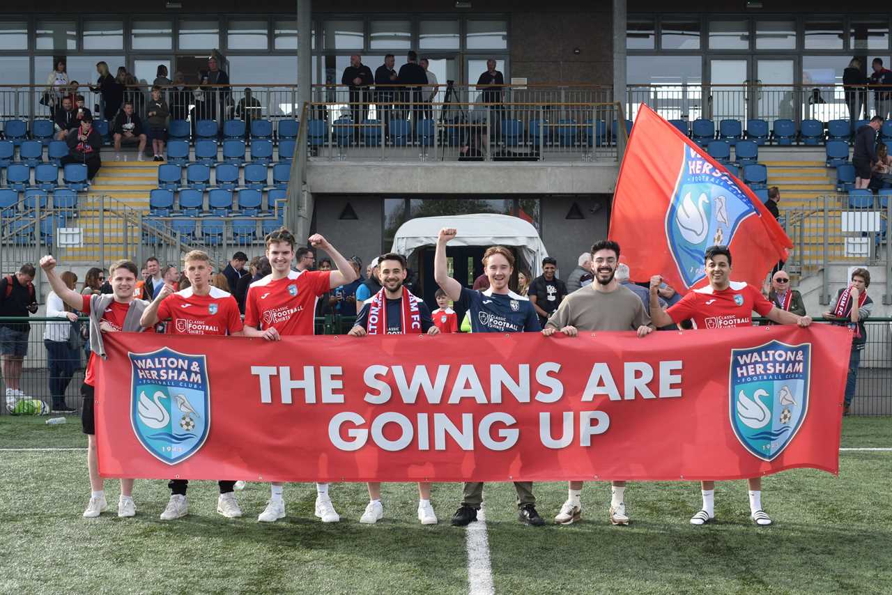 Seven men standing in a line holding a banner declaring their soccer team has been promoted