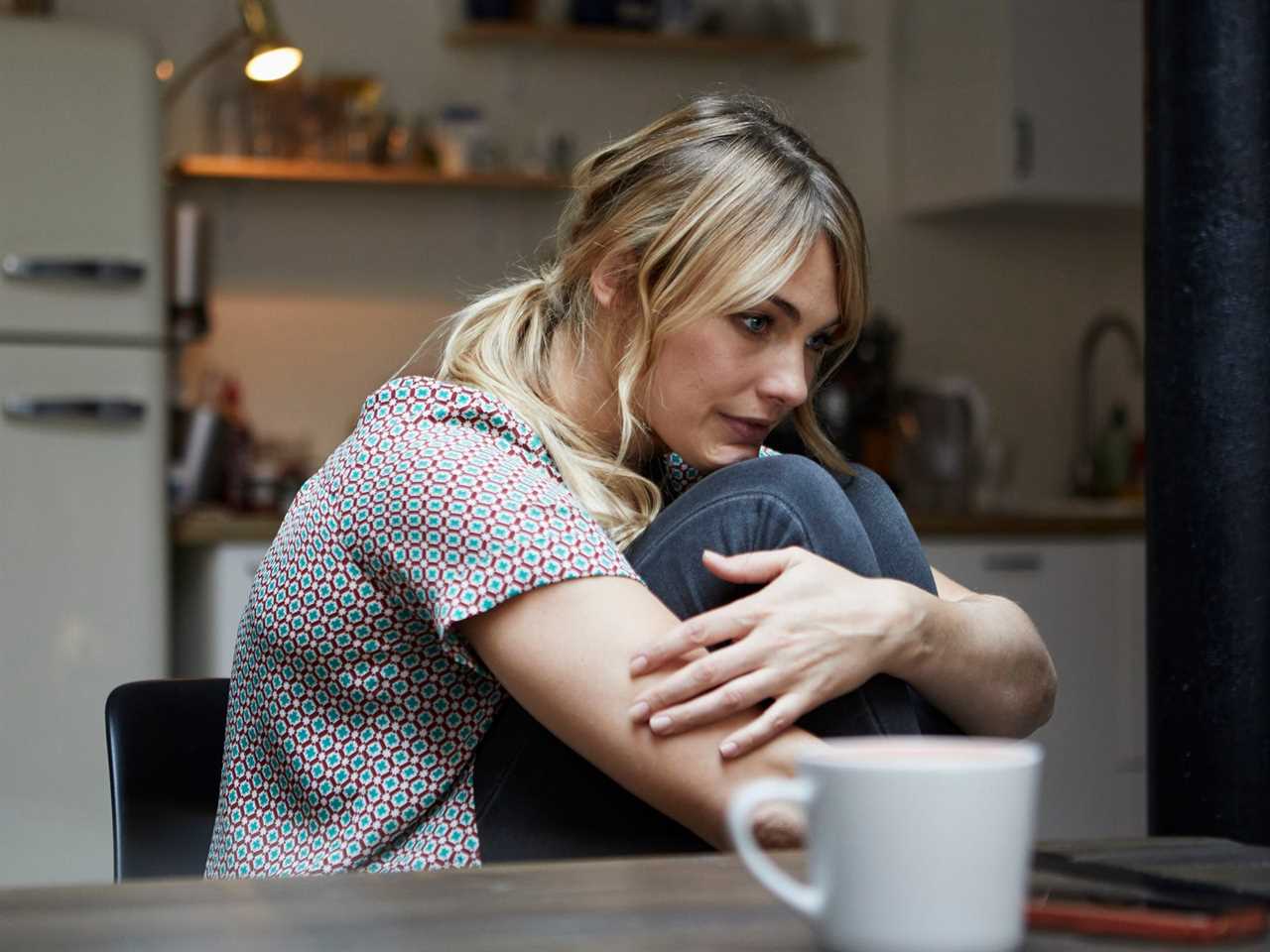 Portrait of pensive woman sitting at table in the kitchen.