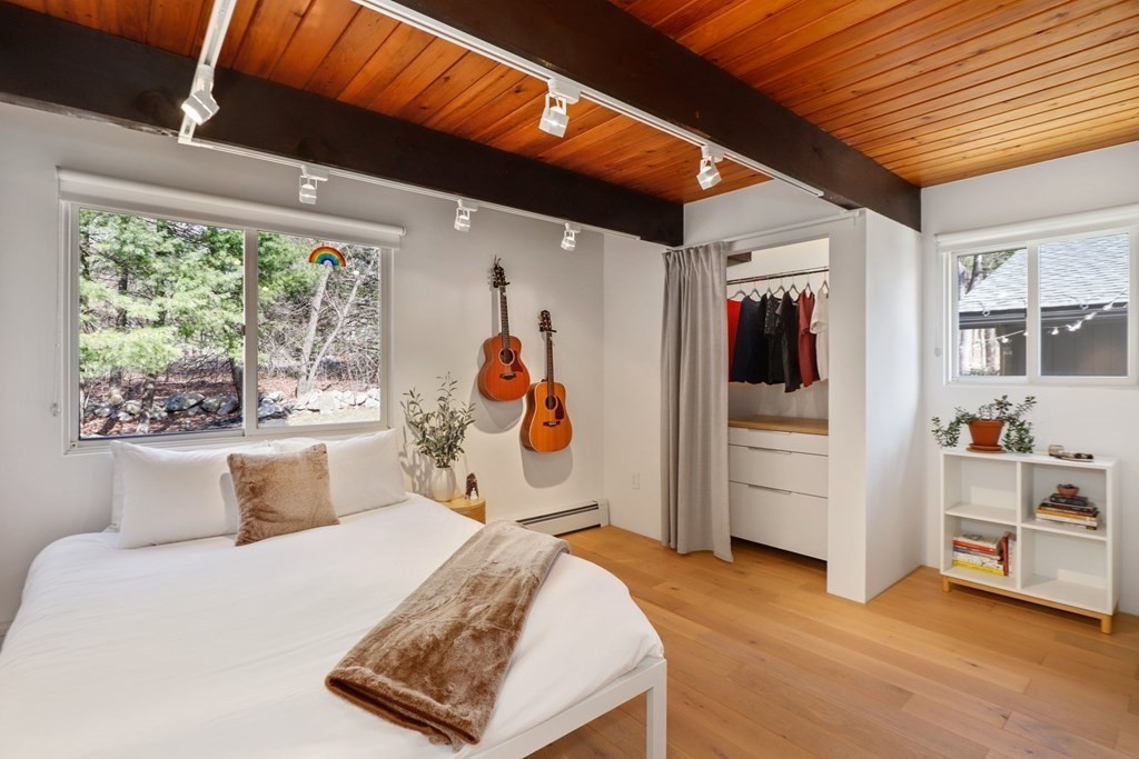 primary bedroom in a cottage with exposed beams, wood floor and nature views