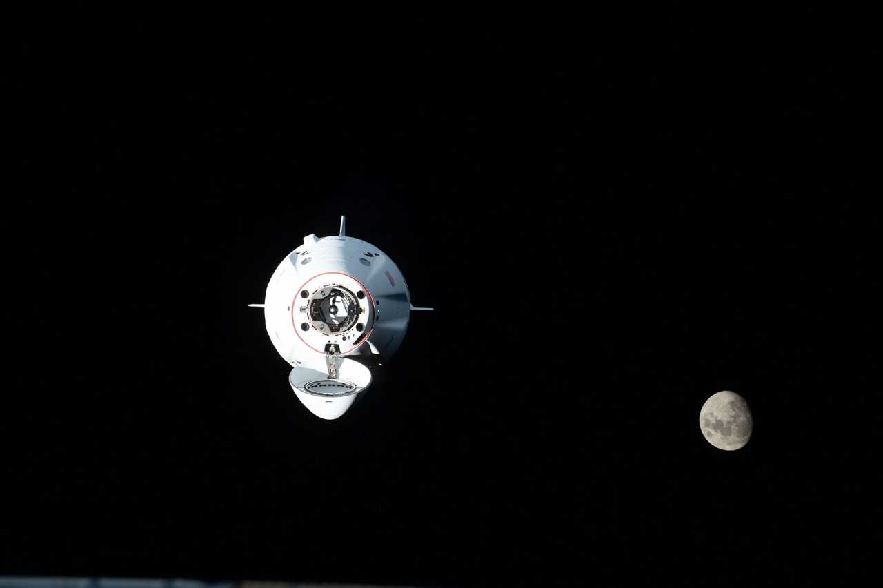 crew dragon spaceship flying in black space with moon in background