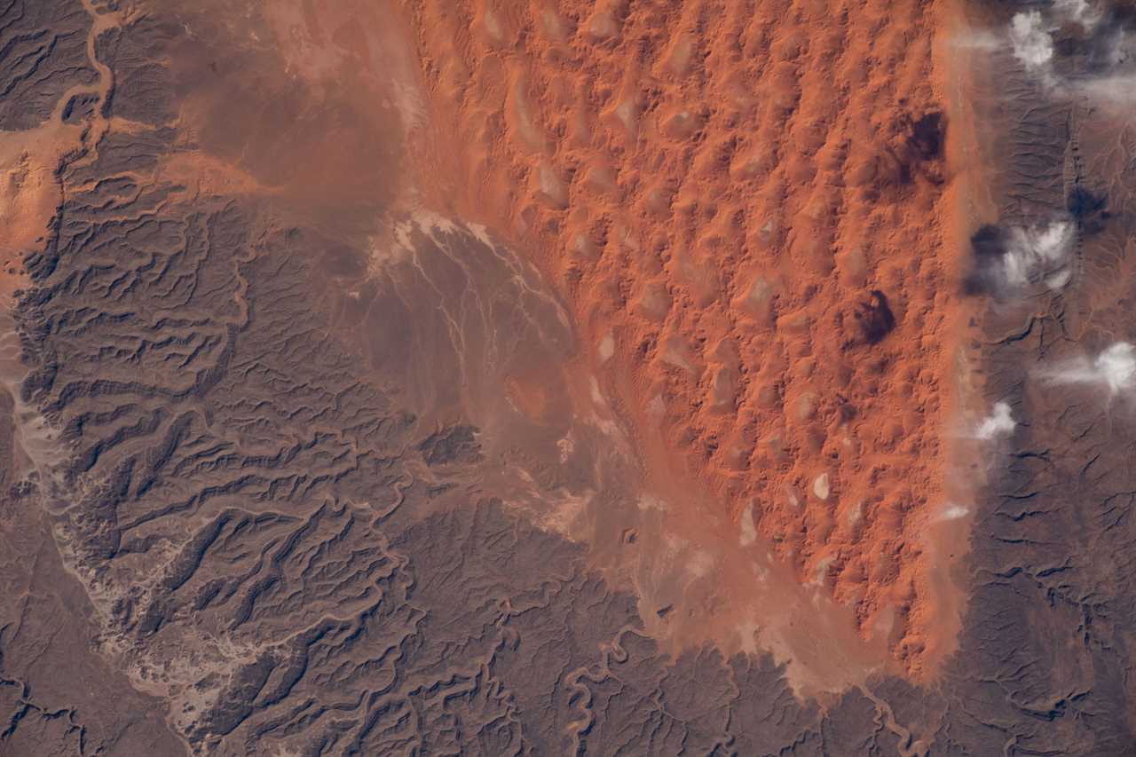 brown craggy rock surrounds red orange sand dunes