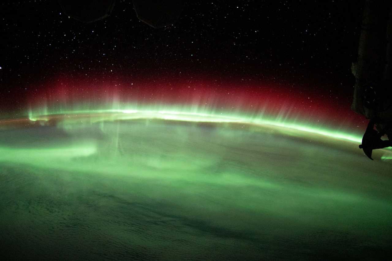 green and red aurora lights stream across earth horizon against black space