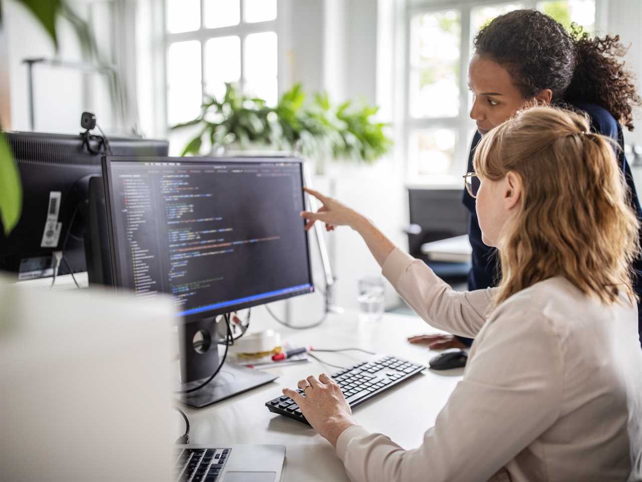 Businesswoman discussing computer program with female colleague at desk in creative office