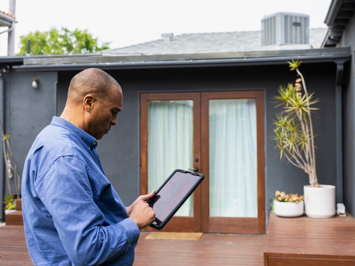 A photo of a home appraiser working on a tablet computer outside of a house.