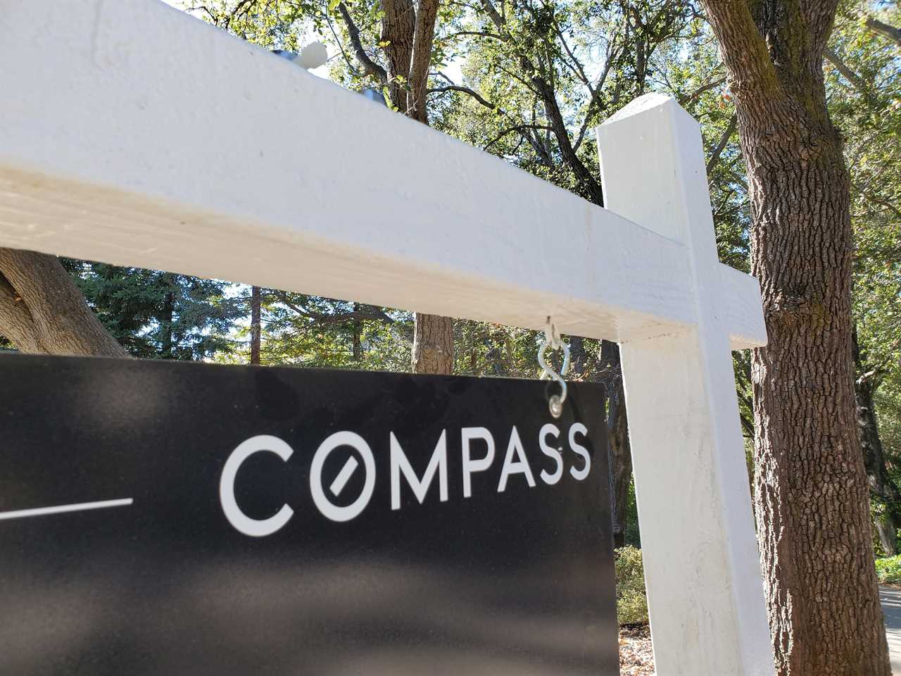 A Compass real-estate sign staked in front of a tree.