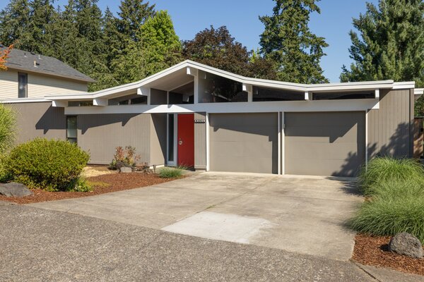 A bright red door extends a warm welcome, popping against the home's neutral exterior. The wide driveway leads to the the two-car garage which merges with front facade.