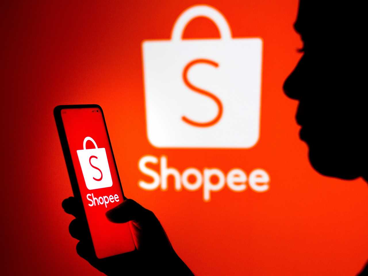 Woman's silhouette holds a smartphone with the Shopee logo displayed on the screen and in the background.