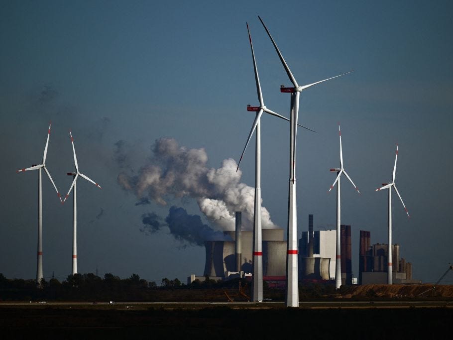 Wind turbines spin in front of a coal-fired power plant.