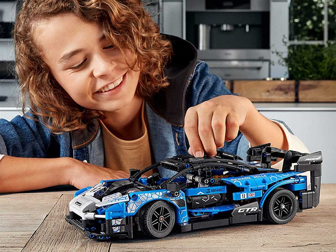 A child playing with an assembled LEGO McLaren car.