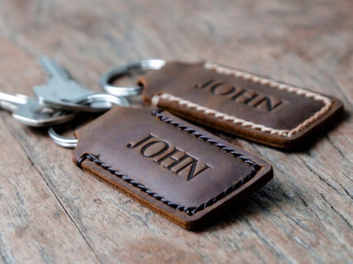 Two sets of keys on a wooden table with personalized leather keychains that read "John".