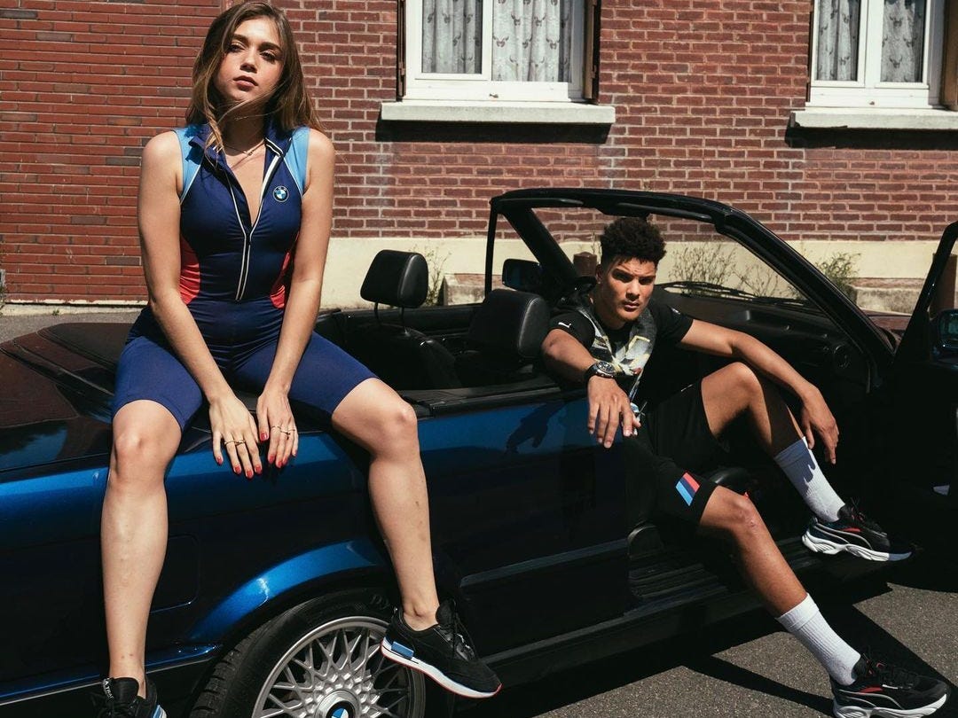 Two people posing next to a convertible wearing the Puma Motorsport branded apparel.