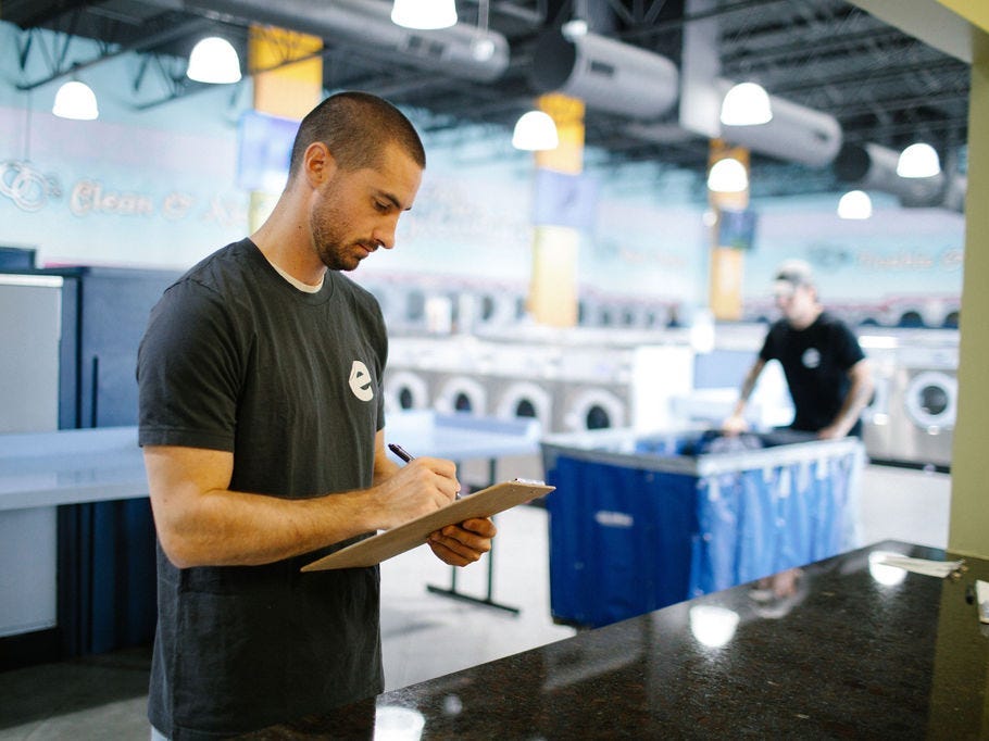 a man writes on a clipboard with a laundromat in the background