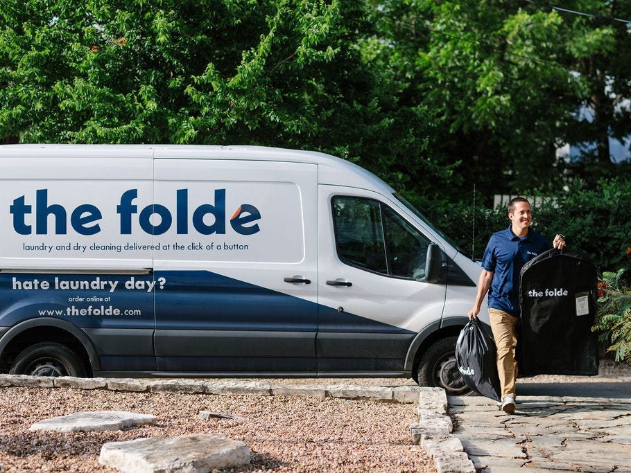 a white van with logo of The Folde is parked in driveway while a man carries a laundry delivery