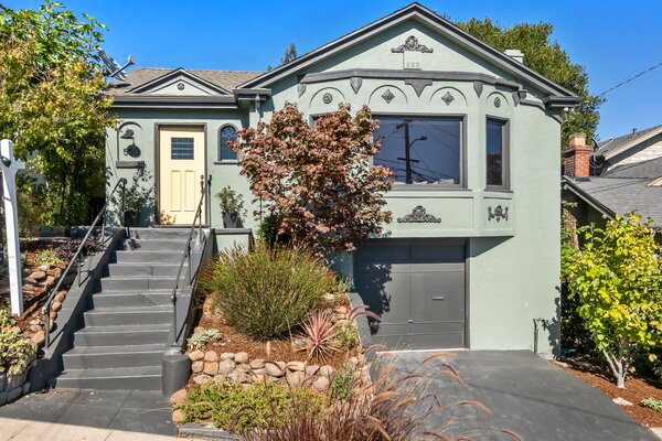 Concrete steps lead to the main entrance on the upper level, where a bright-yellow front door extends a cheerful welcome, all while complementing the home's sage-green facade.