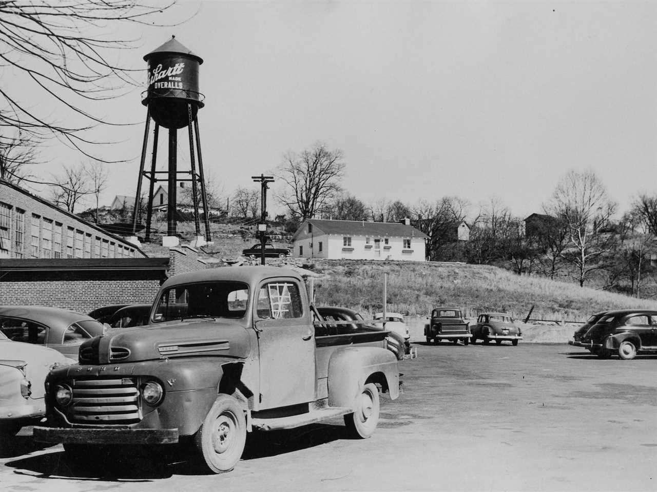 Black and white photo shows Carhartt factory exterior, pickup truck, and water tower