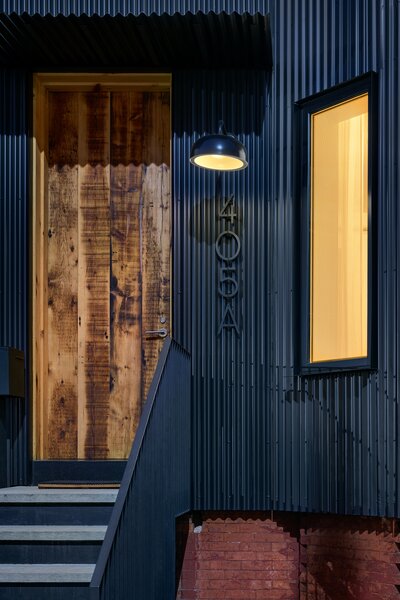 The texture of the reclaimed timber door contrasts with the industrial corrugated steel facade. 