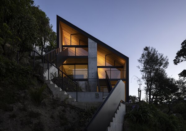 "Named after the metre-thick cast concrete wall separating mirrored dwellings, Party Wall House traces a clean outline on a bush-clad hillside in Wellington. Answering the brief to reimagine density, Ben Mitchell-Anyon and Sally Ogle of Patchwork Architecture subvert a number of notions about duplex living. A singular roof brings elegance to a two-part project and enables efficiency in siting, retaining existing trees for both outlook and privacy."