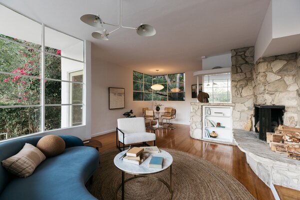 Inside, the light-filled living room is anchored by a gracefully curved stone fireplace, original to the home. Rounded steel casement windows frame views of the nearby Hollywood hills.