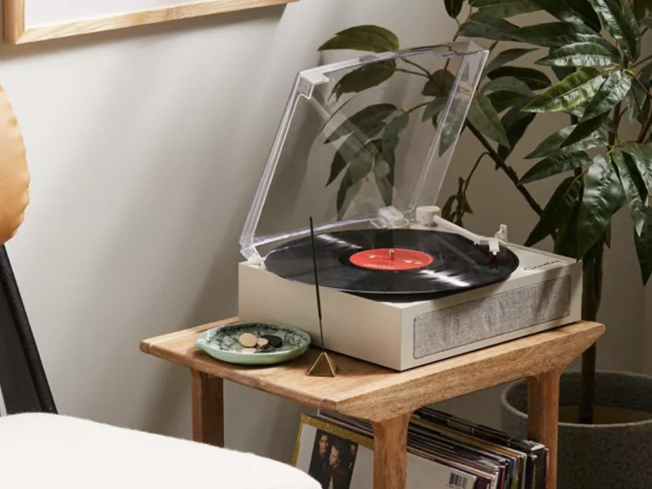 A gray Crosley Urban Outfitters exclusive Ryder Bluetooth record player sitting on a wooden shelf with a stack of records, one of the best gifts for a Taylor Swift fan