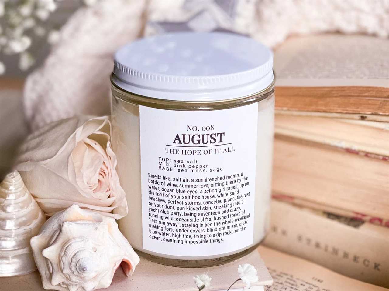 Taylor Swift themed candle from Etsy scented around "August" next to a stack of books, seashells, and flowers, one of the best gifts for a Taylor Swift fan