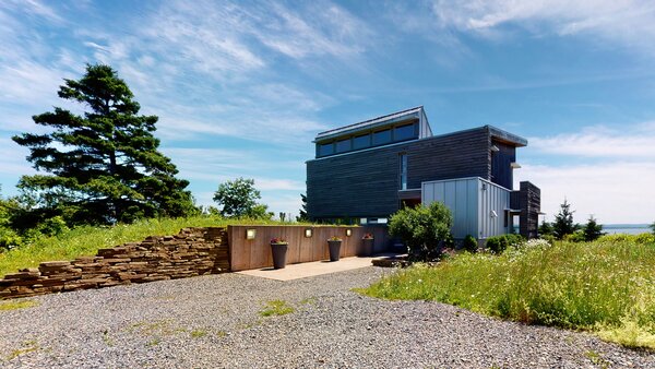 A long gravel driveway leads to the two-level home, which sits nestled away from the road on a spacious coastal lot, surrounded by soaring trees and a meadow-like yard.