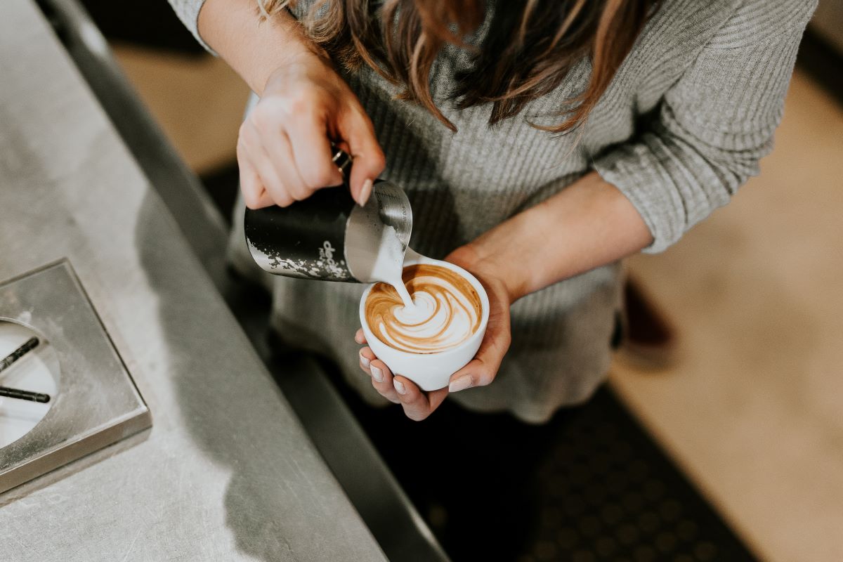 person pouring cream into a coffee cup