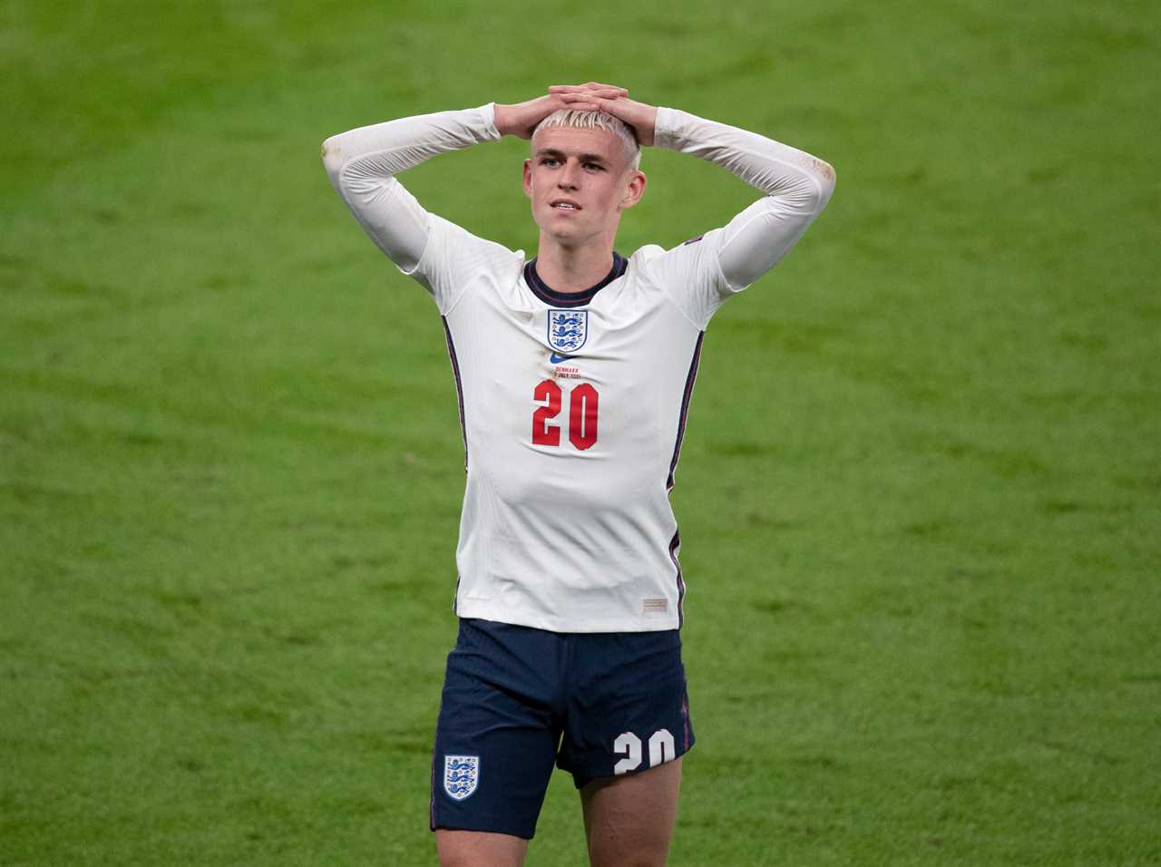 Soccer player Phil Foden stands with his hands on his head on a soccer pitch