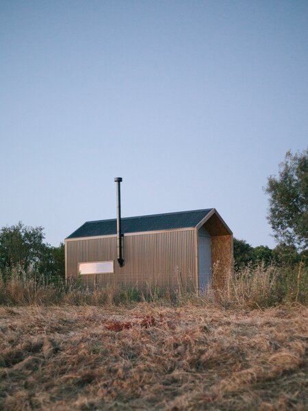 The cabin is clad with corrugated metal panels. The rectangular window is positioned over the kitchen to let in light and air.