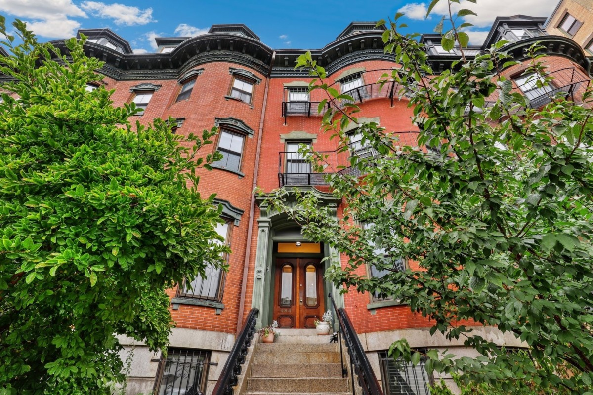 red exterior row home with a stoop and trees outside