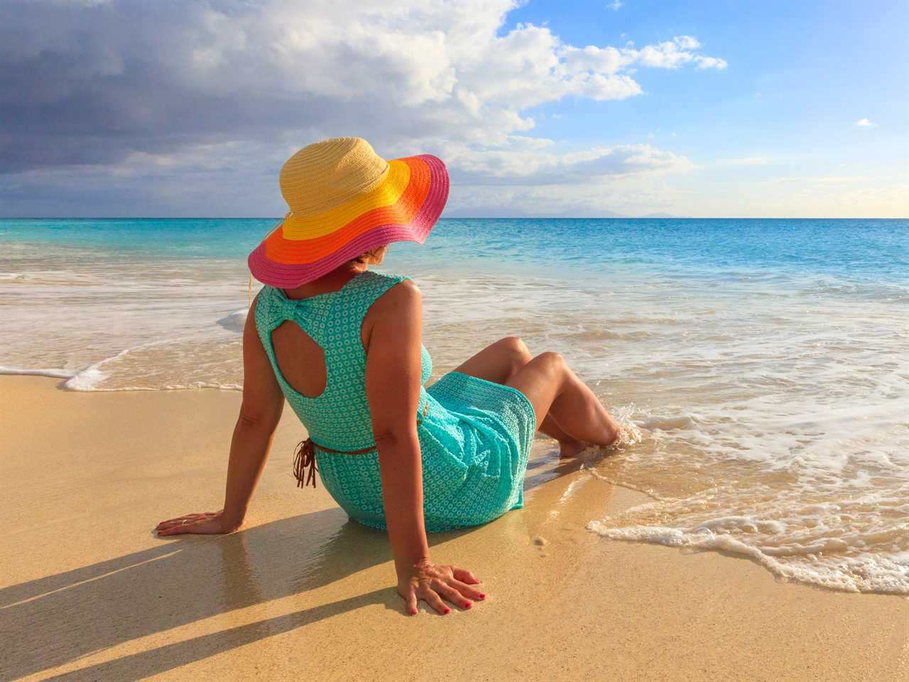 Woman with hat sits on seashore, Ffryes Beach, Antigua, Antigua and Barbuda, Caribbean, Leeward Islands, West Indies