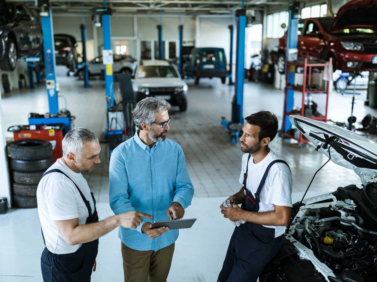 Manager using digital tablet while talking to mechanics in auto repair shop