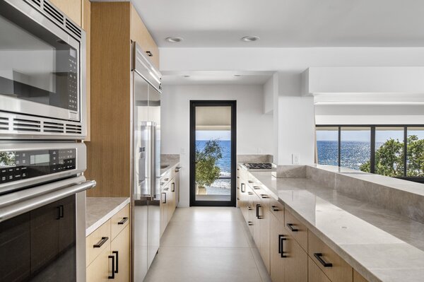 The light-filled kitchen features top-of-the-line appliances, as well as extensive worktops, capped with marble. A tall, black-framed glass door provides direct outdoor access.