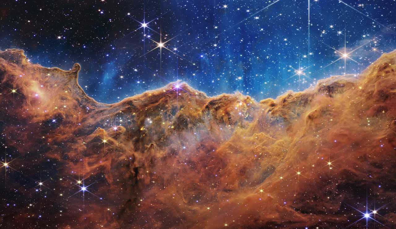 carina nebula star-forming region orange brown clouds of gas and dust with stars against bright blue background