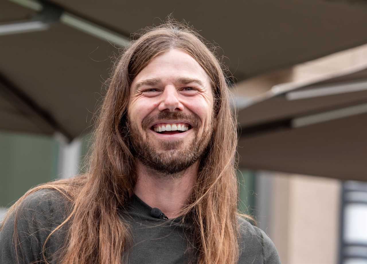 A close-up of a man with long hair who is smiling.