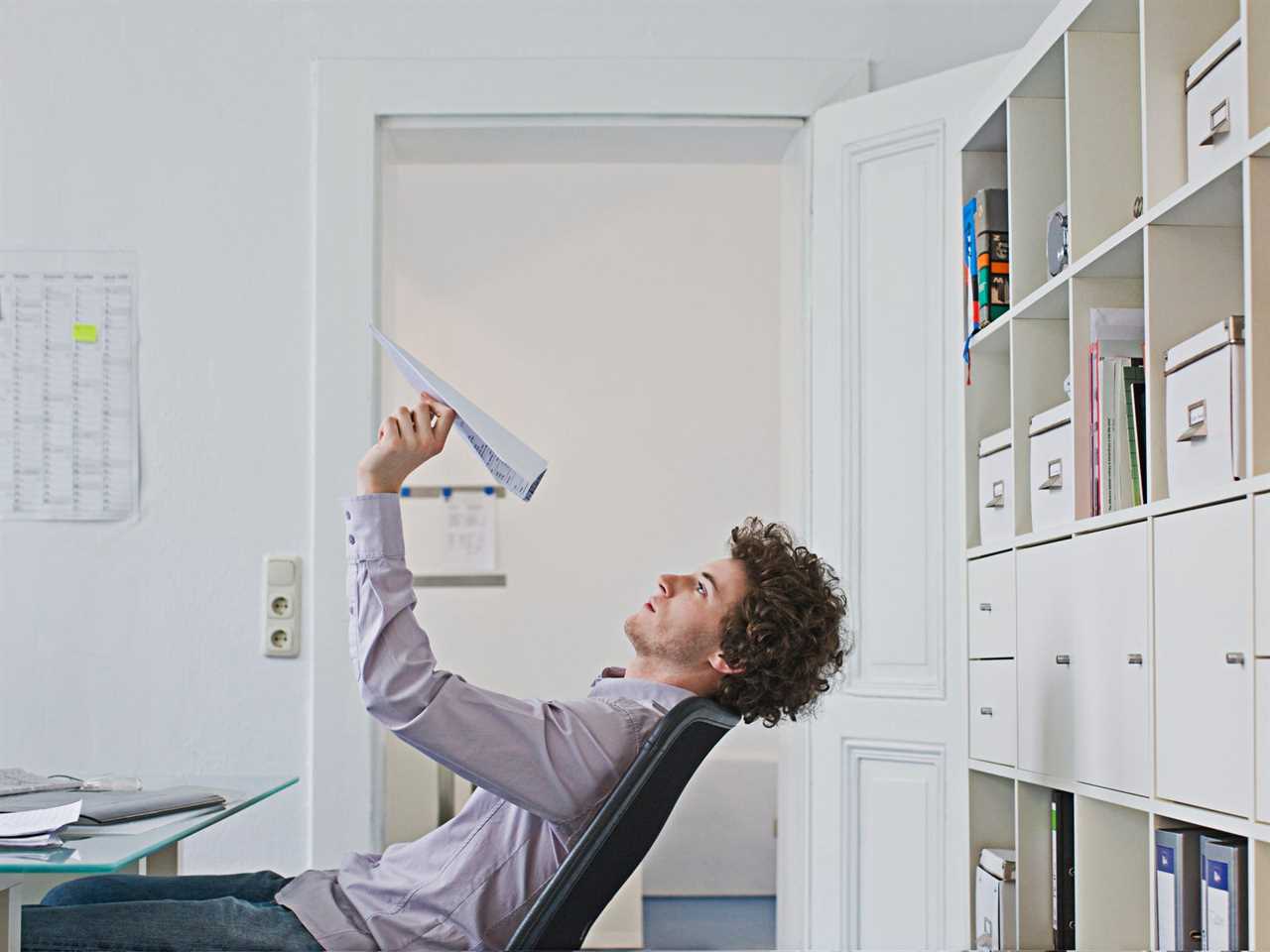 A businessman plays with a paper airplane in the office.