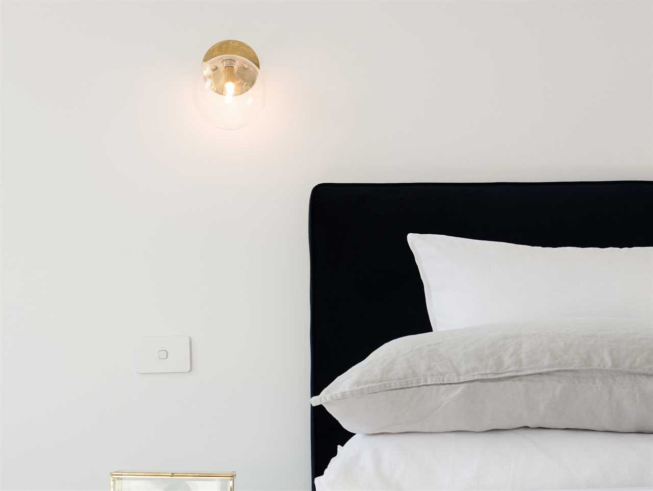 A bed with gray and white sheets with a lit sconce next to it