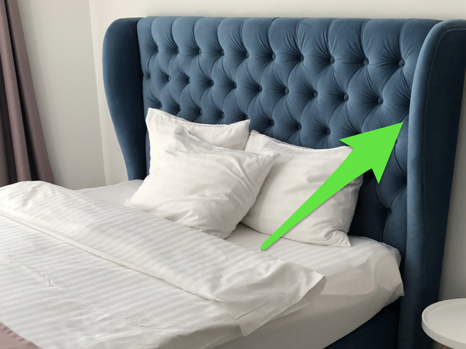 A bed with white sheets and a blue, curvy headboard with a green arrow pointing to headboard