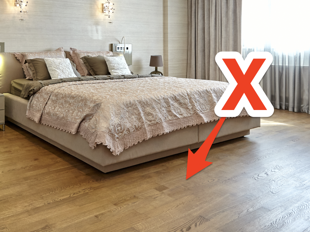 Bed with bare wooden floors and red X and arrow pointing to floor