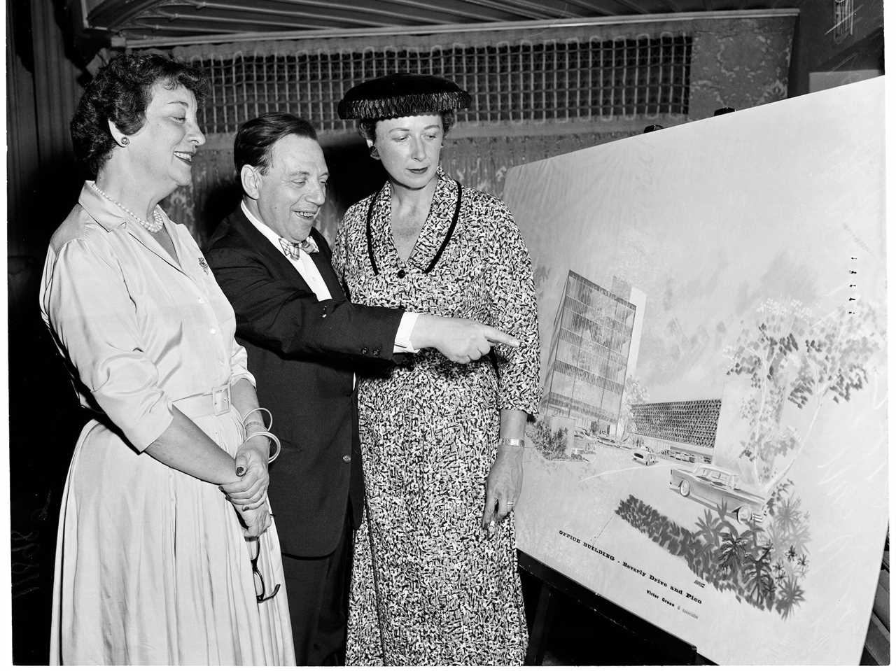 Victor Gruen stands between two women while pointing at an architectural rendering