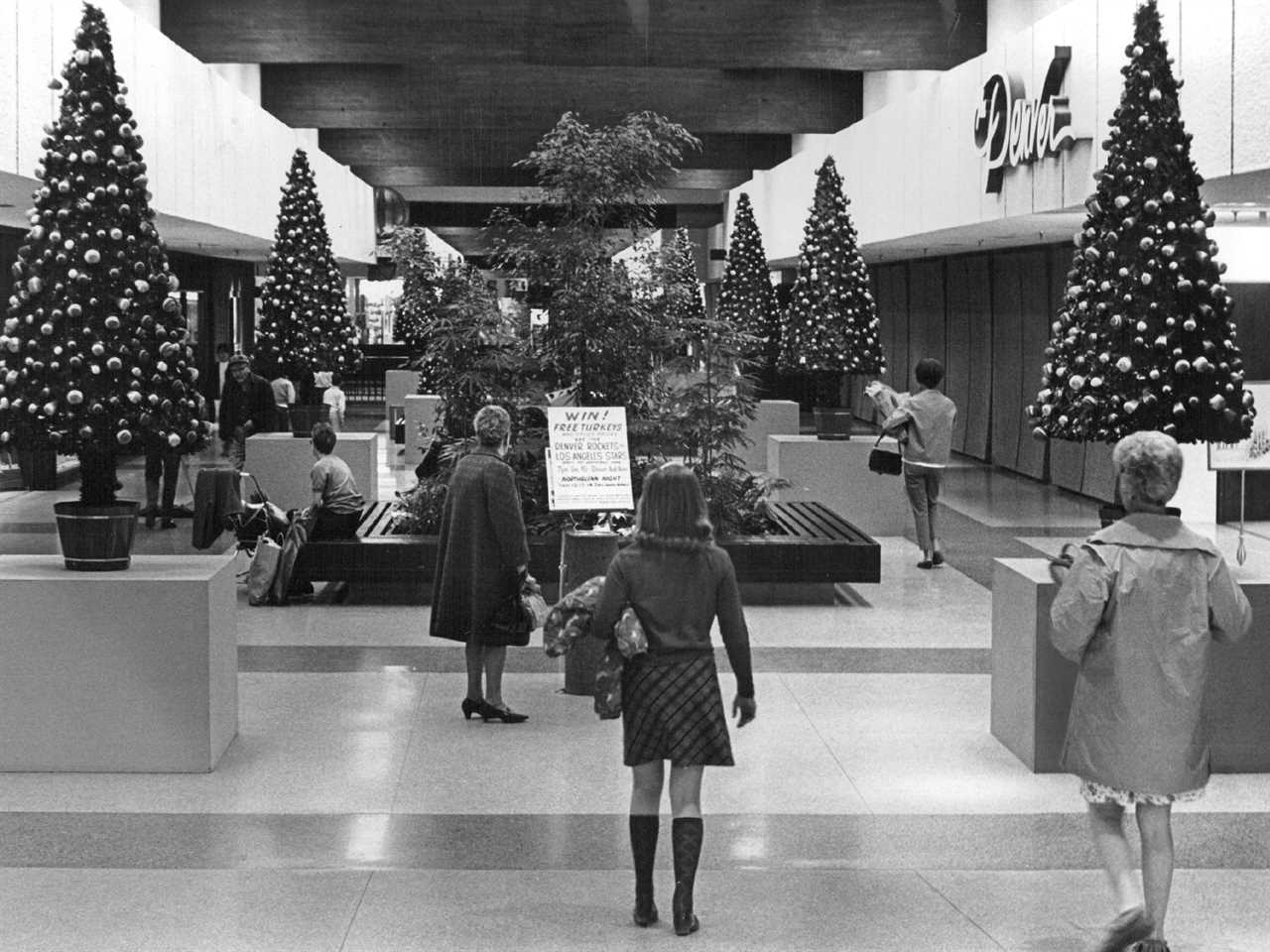 Shoppers walk amid decorated Christmas trees inside shopping mall in the 1960s