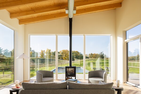 Inside, tall ceilings enhance the sense of space, while expansive windows frame striking views of the rolling hills in the backyard. A black wood stove anchors the main living room.