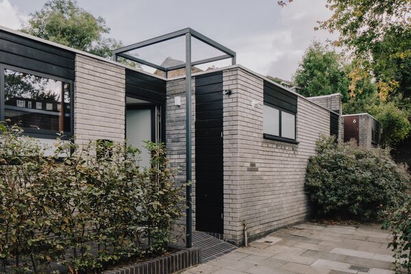 Striking black soffits and window frames contrast with the light colored brick facade. An elegant glass portico above the main entrance adds modern flair to the 1960s structure.