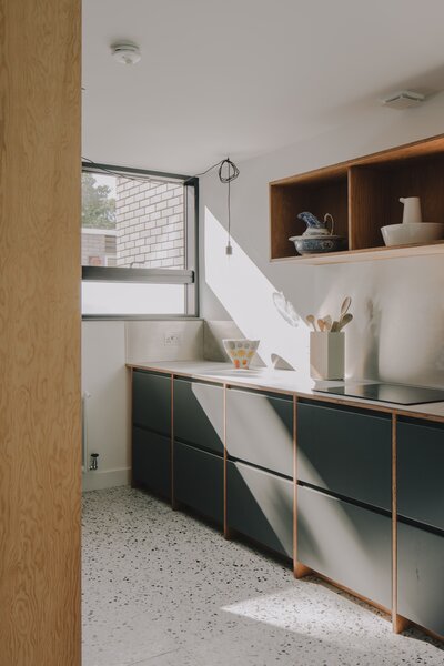 Inside, the kitchen wraps around the front corner of the single-story layout. Expansive glazing allows a seamless flow of light inside, which reflects off the white terrazzo floors.