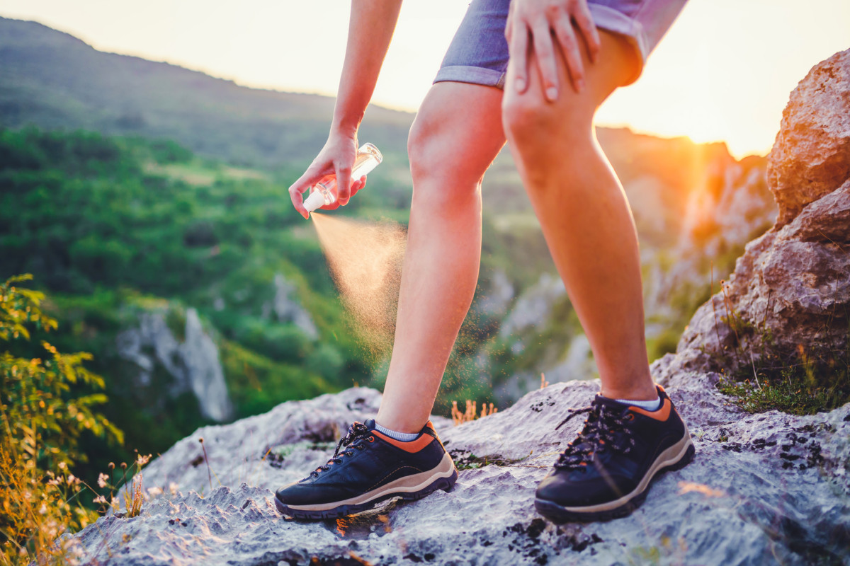 Woman using anti mosquito spray outdoors at hiking trip Getty