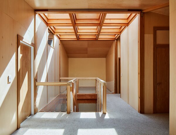 The emphasis on wood finishes continues inside, where the skylit atrium bifurcates the house. On the second floor, the primary bedroom and a pair of smaller bedrooms straddle the stairwell.