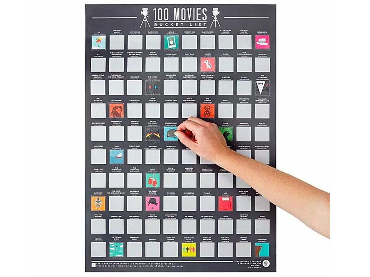 A hand scratching off a square on a black poster with 100 scratch off squares that display movie posters