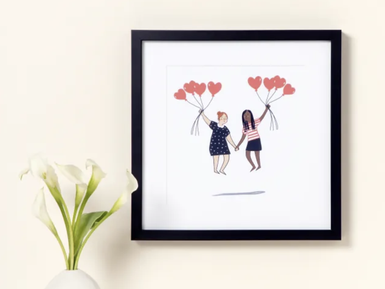 Custom illustrated portrait of two people holding hands while floating from a bunch of heart-shaped balloons hanging in a frame on a wall with a vase of flowers below it.