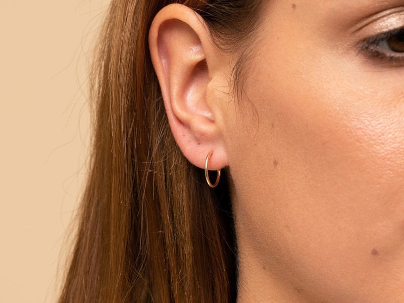 Closeup of a person's ear wearing a Mejuri small gold hoop earring