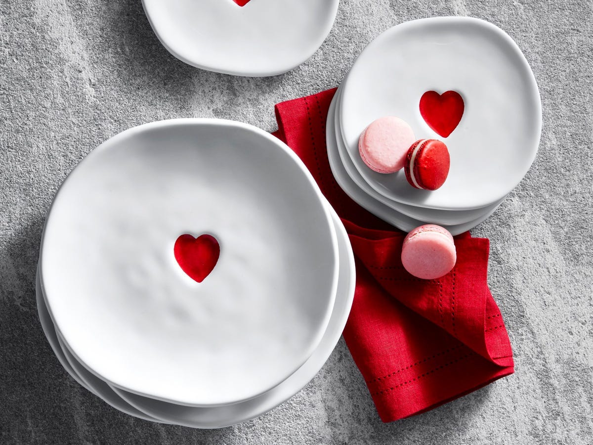 Two stacks of dinner and salad white plates with a red heart indent in the center, and three macarons on top of the stack.