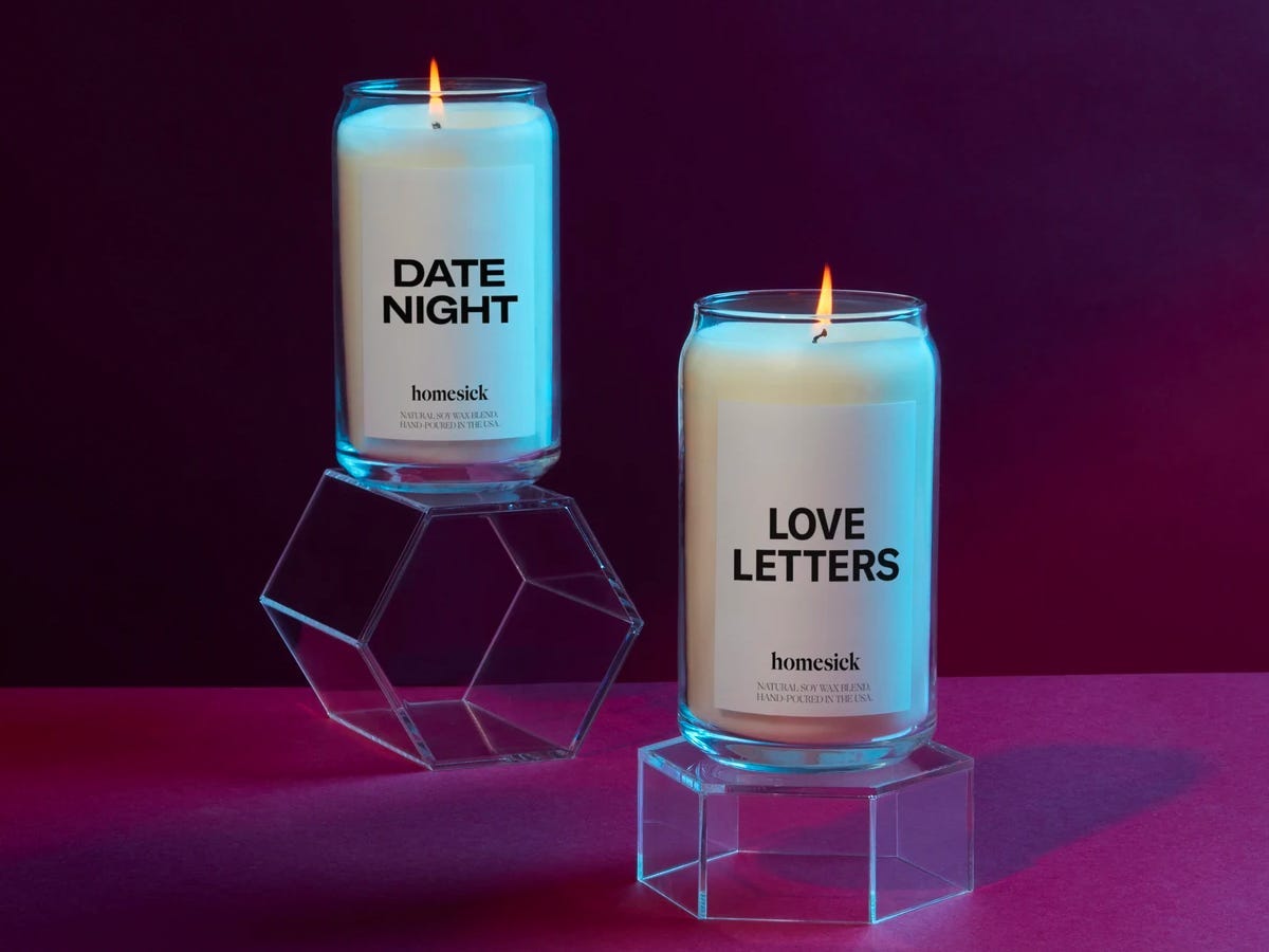 Two lit Homesick candles in the scents Love Letters and Date Night set on top of clear stands.